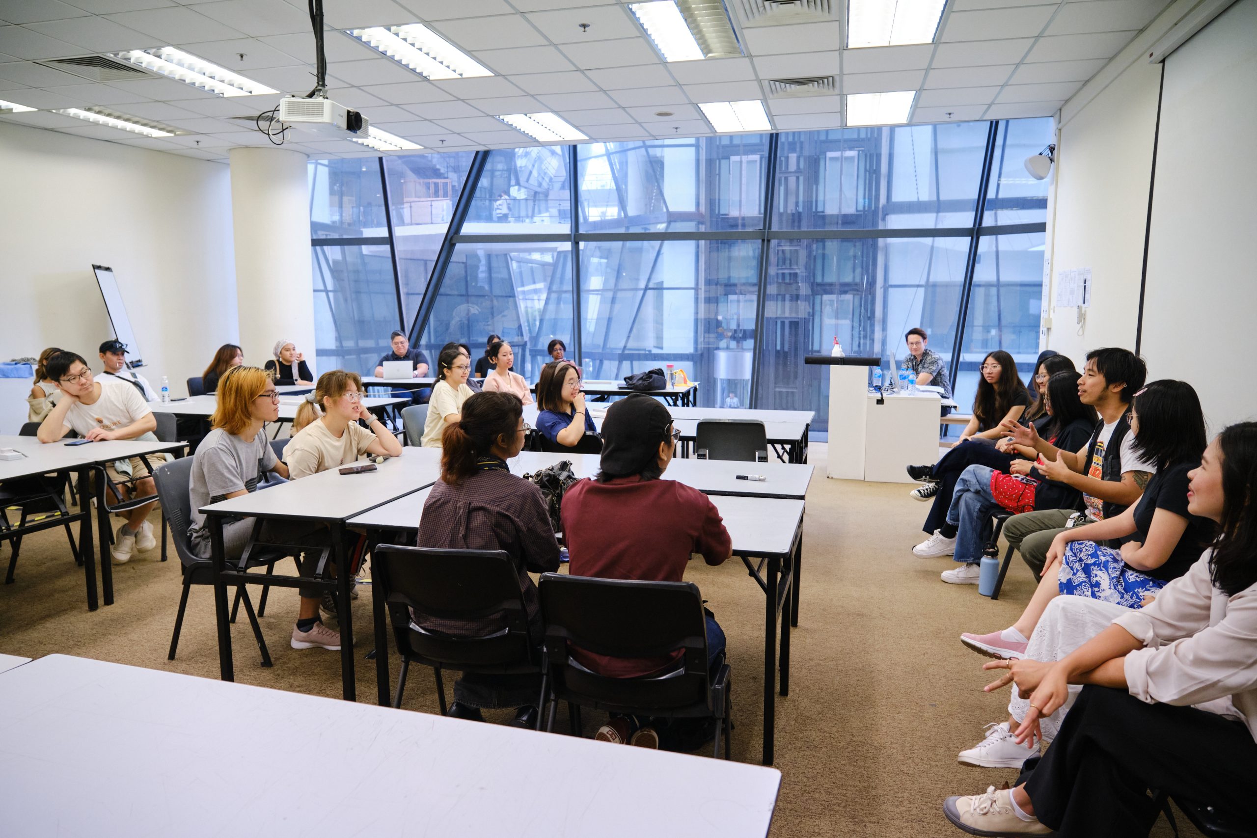 Students listen attentively to a panel discussion in a brightly lit LASALLE classroom with floor-to-ceiling windows.