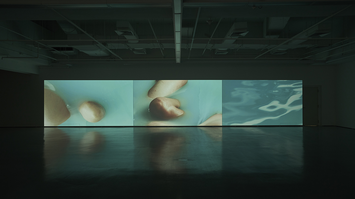 Immersive video installation with floating limbs and rippling water, evoking sensory depth and contemporary expression