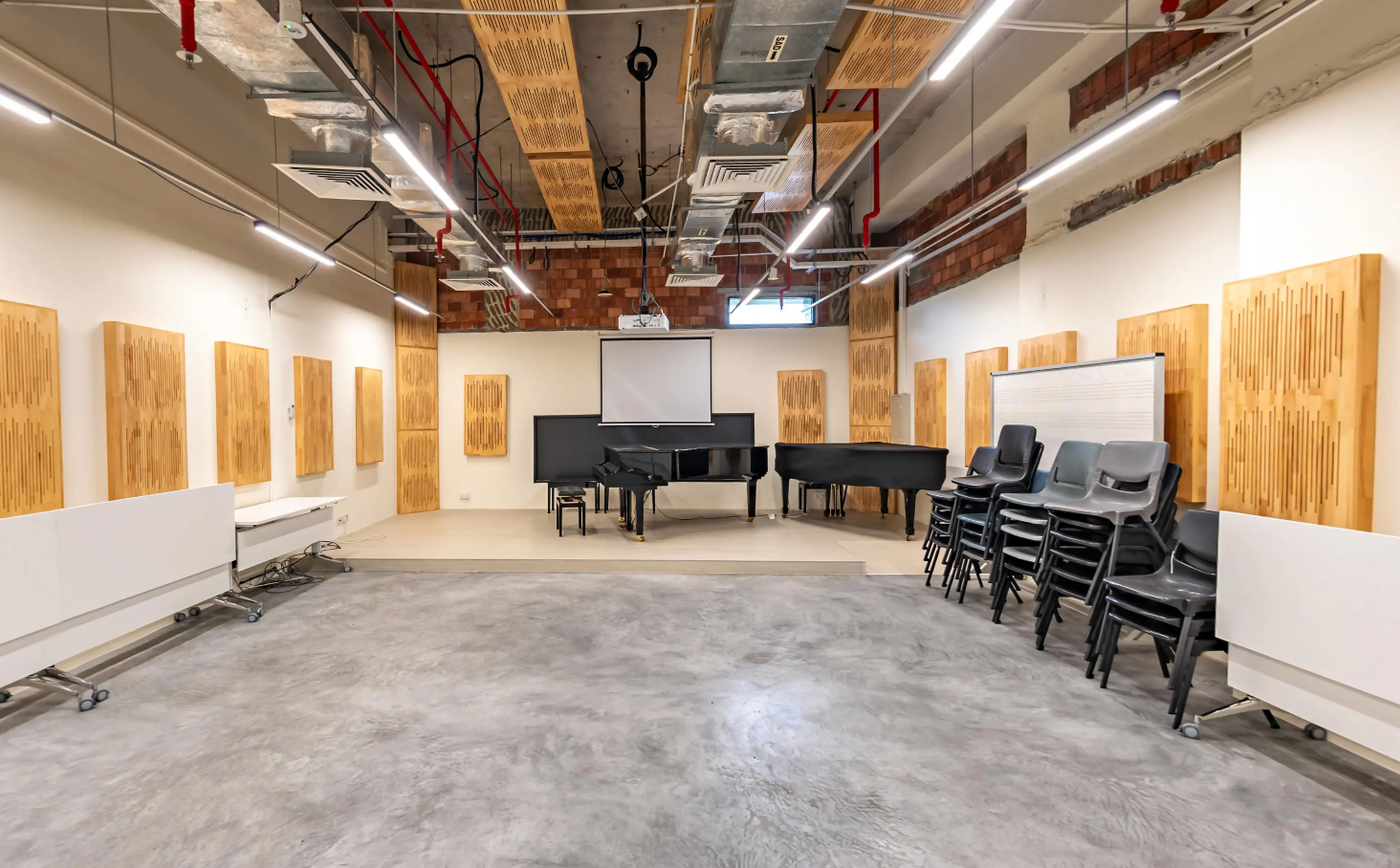 A music studio with two grand pianos, acoustic wall panels, and stacked chairs in a spacious setting.