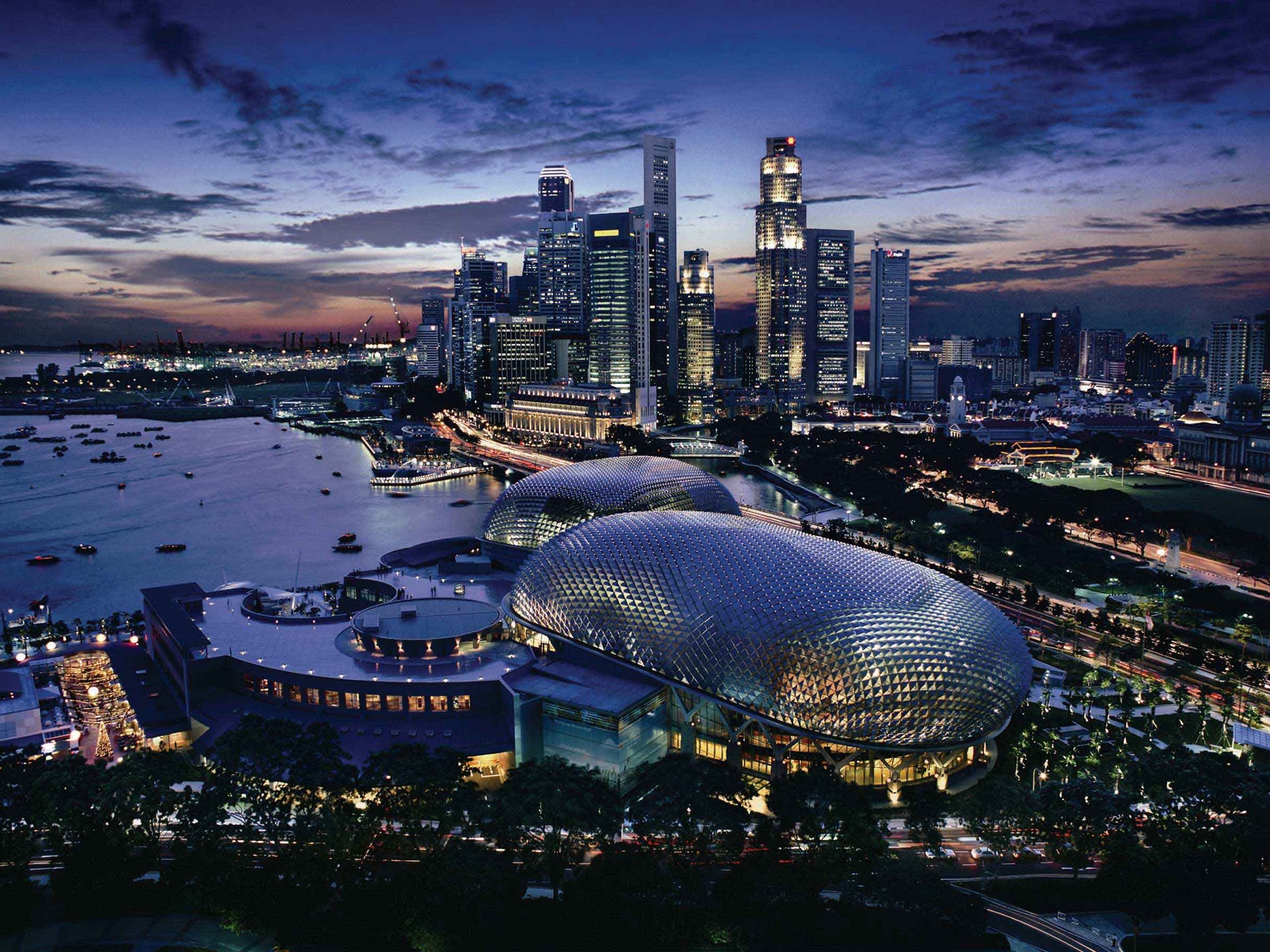 Aerial view of Singapore’s Marina Bay skyline at dusk, with skyscrapers lit against a deep blue sky and the Esplanade domes visible in the foreground.