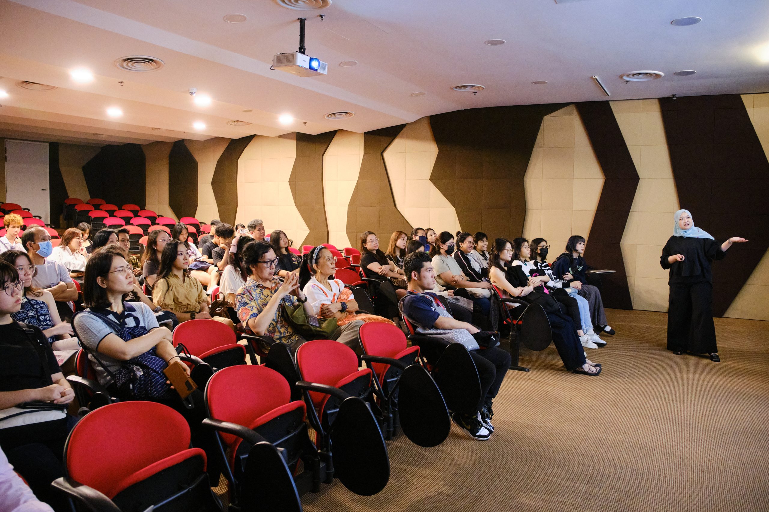 Audience seated in a LASALLE lecture theatre with red chairs, listening attentively to a speaker presenting at the front of the room.