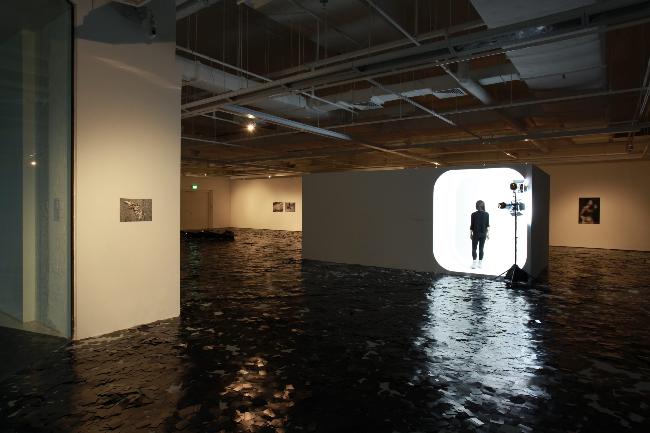 LASALLE gallery with dark reflective flooring, featuring a glowing white cube installation where a person stands inside.
