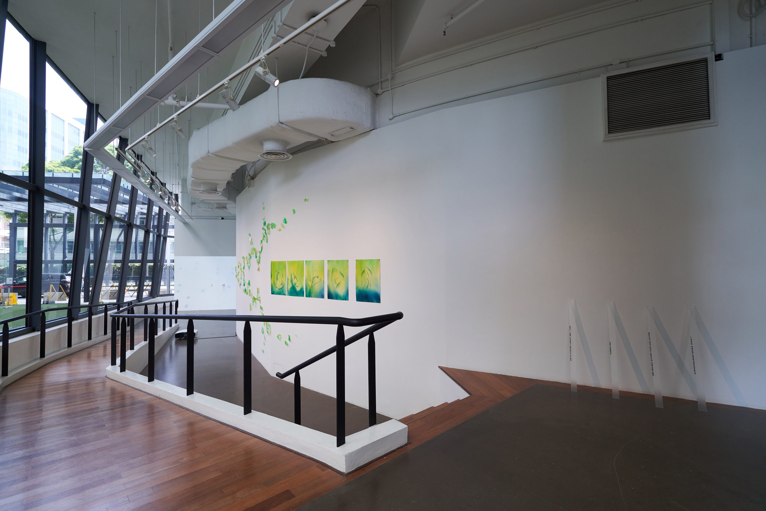 LASALLE gallery walkway with green and blue abstract paintings on a curved white wall, accented by scattered wall decals and natural light.