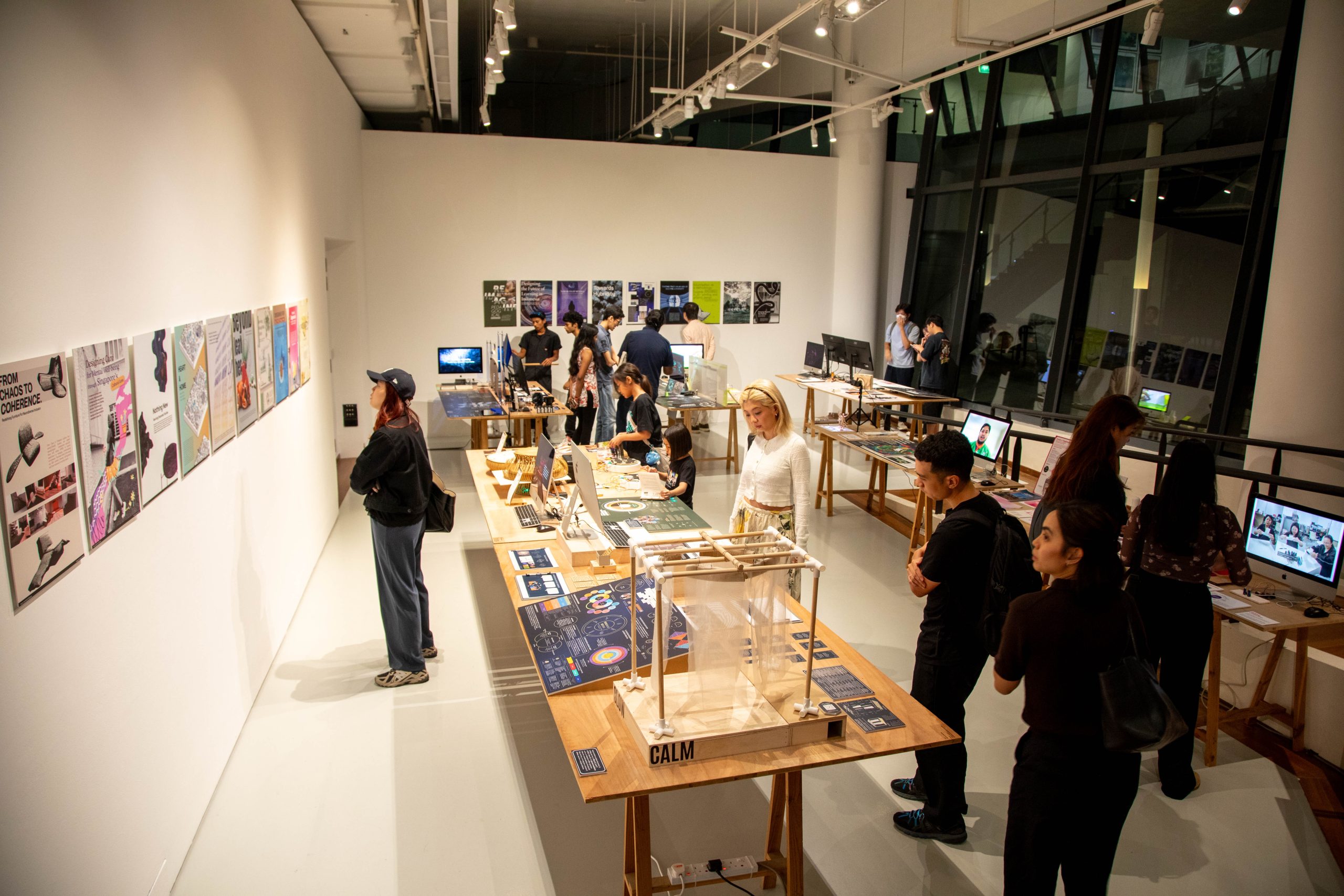 Visitors explore LASALLE exhibition of student design projects, with posters, prototypes and digital displays arranged on tables.