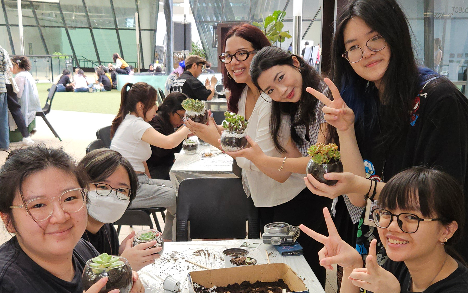LASALLE students smile while holding DIY succulent terrariums during a hands-on workshop at the outdoor campus courtyard.