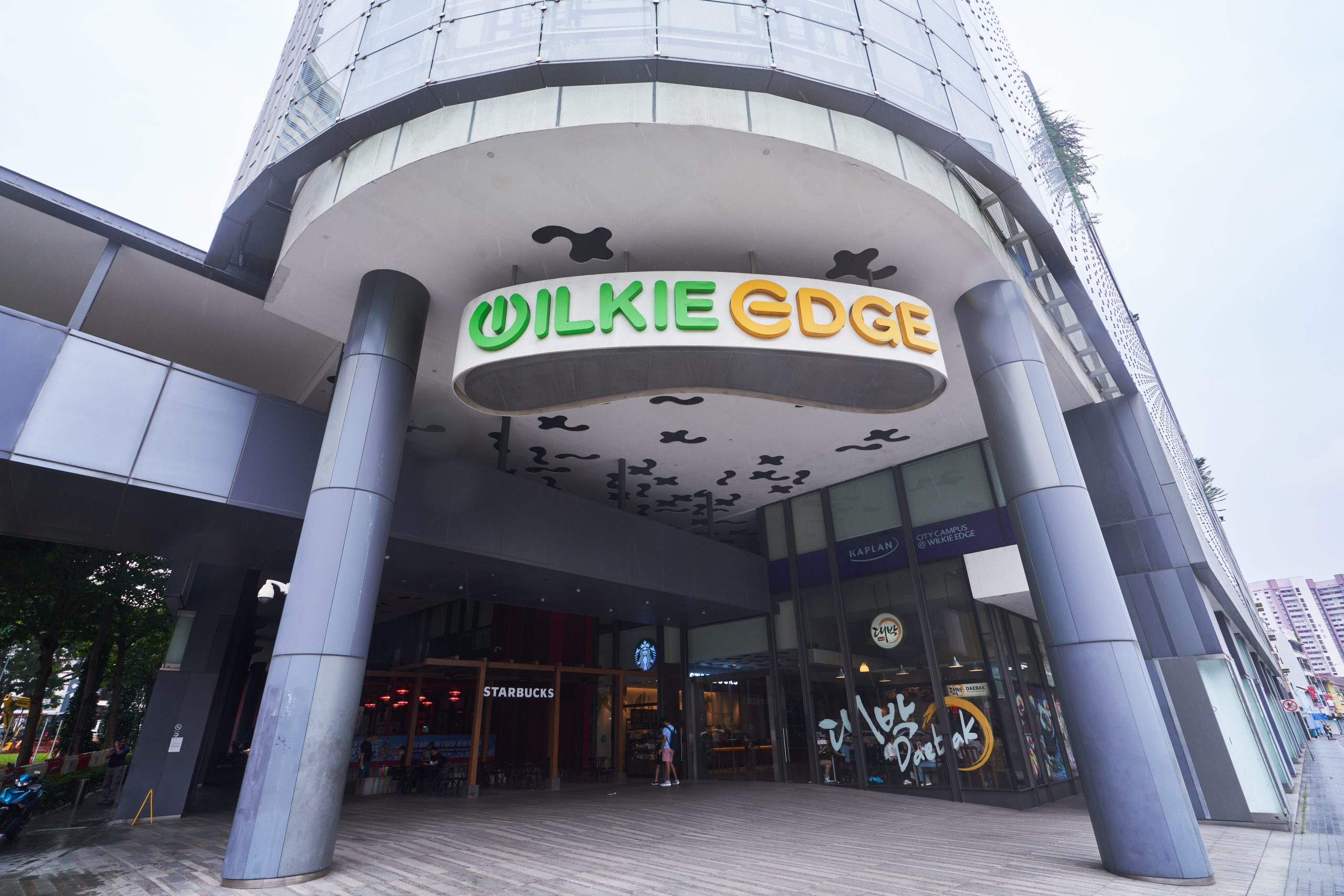 Exterior of Wilkie Edge building with its curved canopy, bold signage and visible street-level cafés.