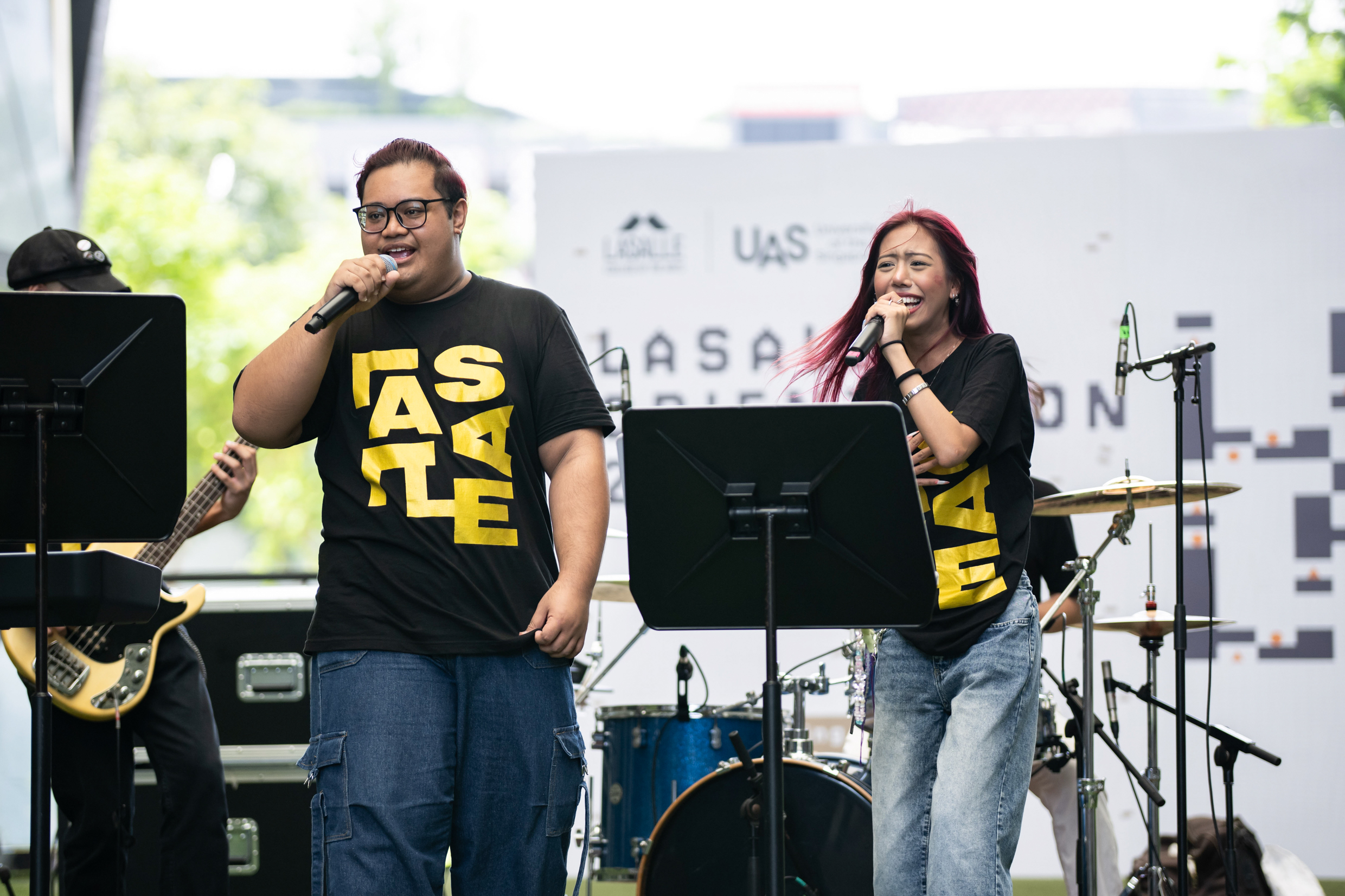A diverse group of people joyfully singing together at an outdoor event, surrounded by trees and a festive atmosphere.