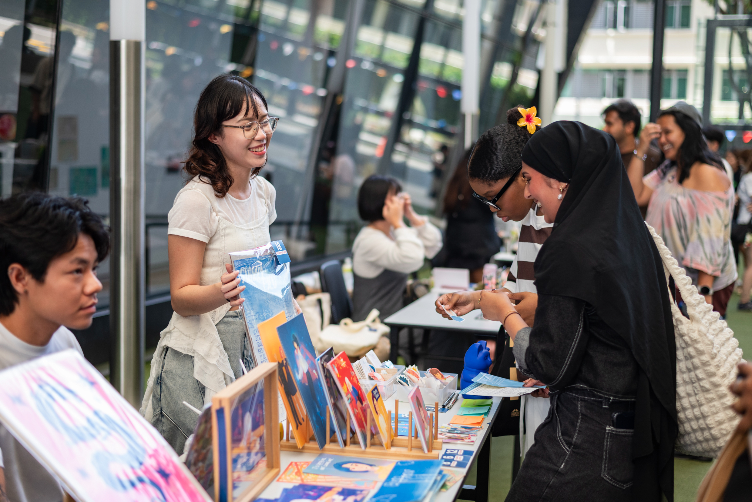 A group of people gathered around a table displaying various paintings, engaged in discussion and observation.