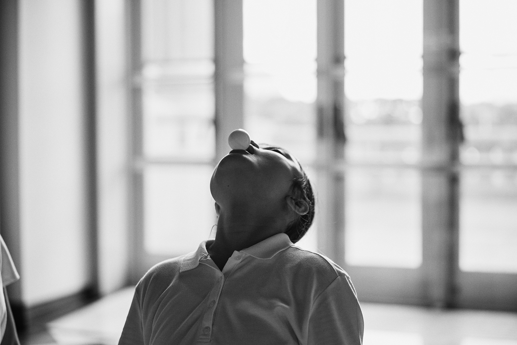 A student bends backwards, ping pong ball balanced on her lips.